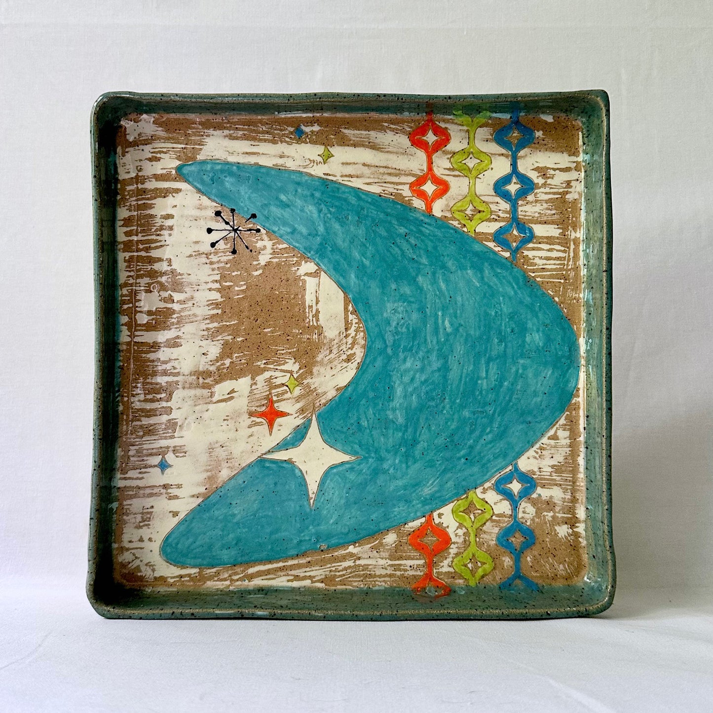 Decorative plate with a blue mid century boomerang and starlite design on a textured brown background