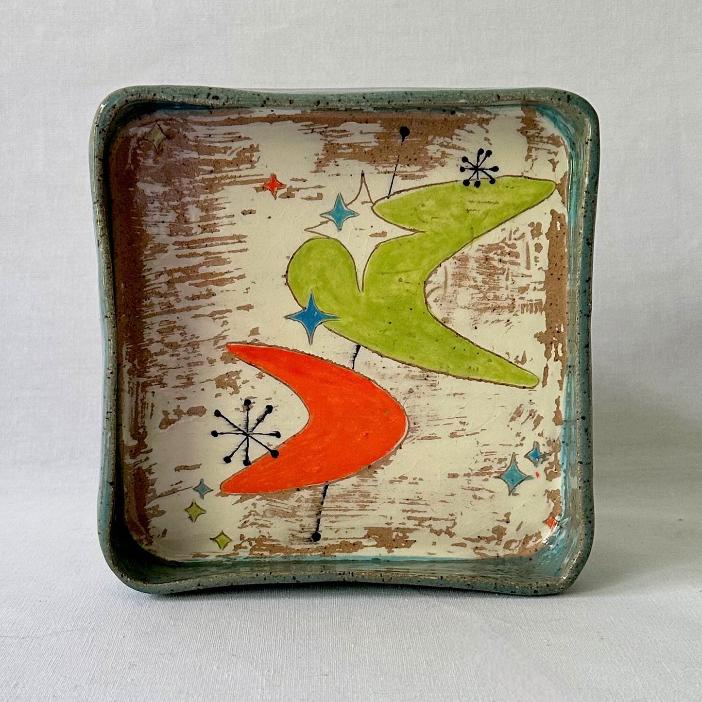 Decorative tray with mid century design featuring a green and orange boomerang on a textured surface.