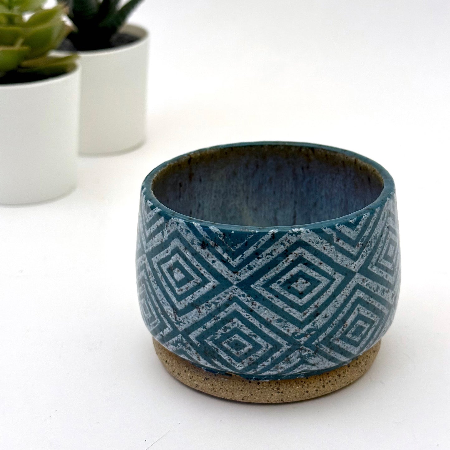 Small handmade ceramic planter in rich teal glaze with bold geometric diamond pattern and speckled stoneware base.