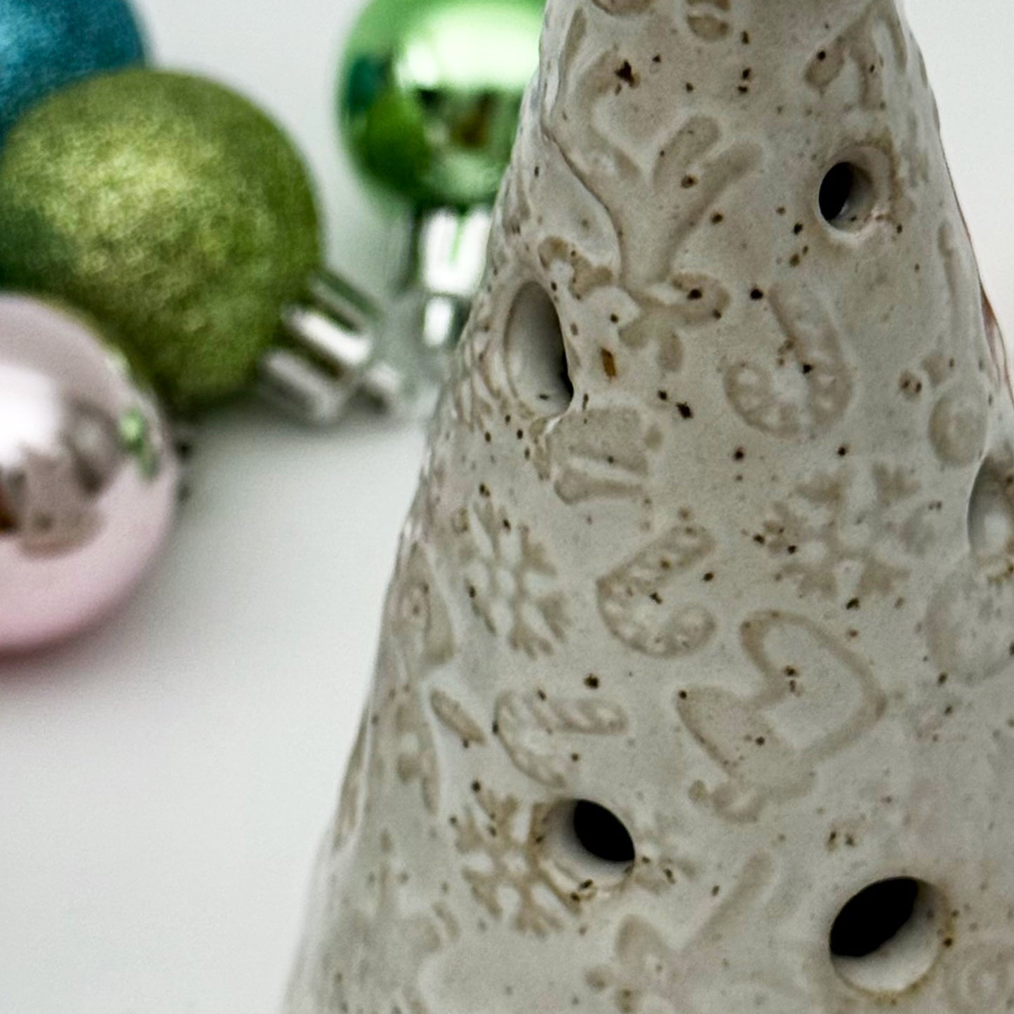 close- up of Decorative ceramic christmas tree luminary with a star on top, with colorful Christmas ornaments in background.