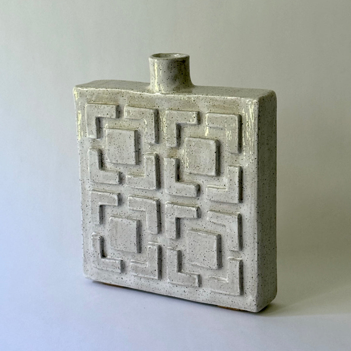 A rectangular ceramic vase with a short cylindrical neck and a raised geometric breeze block pattern on the front, shown on a plain light gray background.
