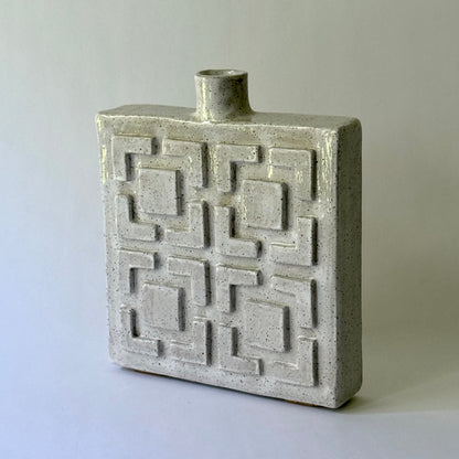 A rectangular ceramic vase with a short cylindrical neck and a raised geometric breeze block pattern on the front, shown on a plain light gray background.
