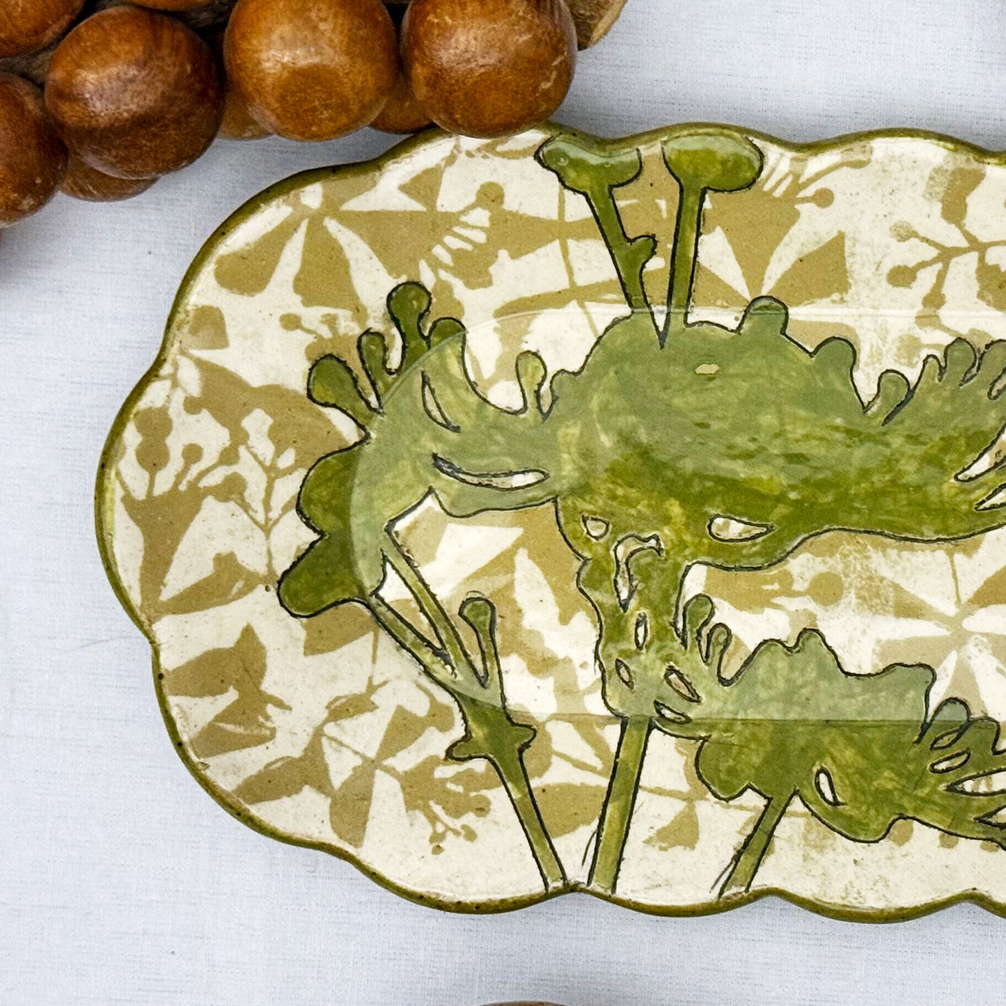 Decorative ceramic plate with olive green floral design on a beige and brown patterned background