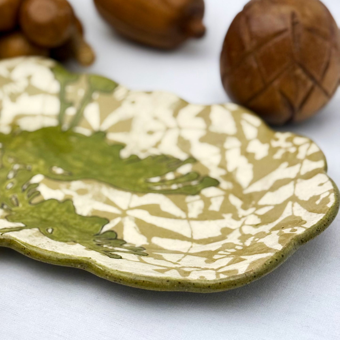 Decorative ceramic plate with olive green floral design on a beige and brown patterned background
