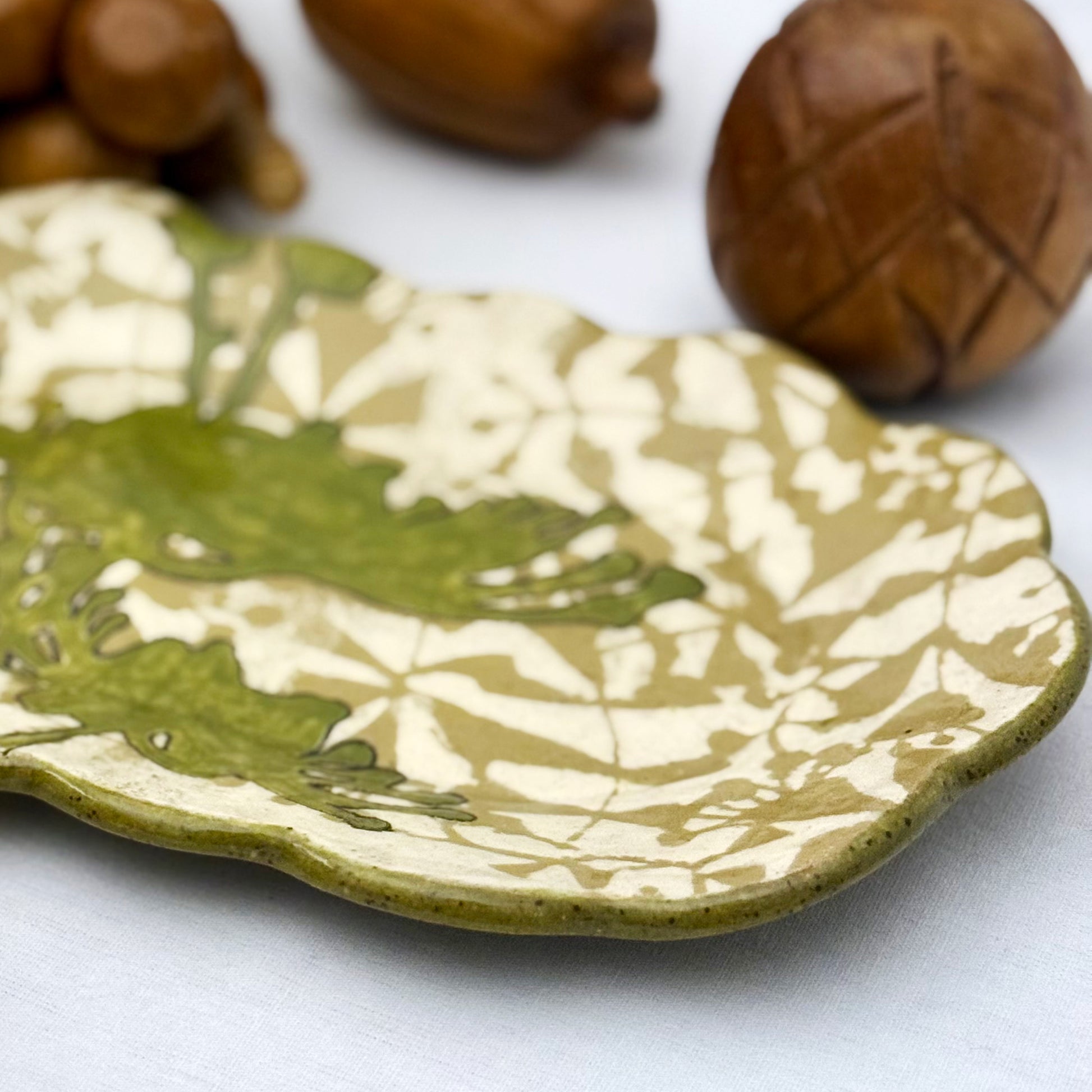 Decorative ceramic plate with olive green floral design on a beige and brown patterned background