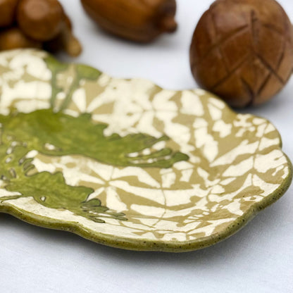 Decorative ceramic plate with olive green floral design on a beige and brown patterned background