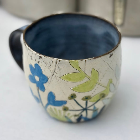 Ceramic mug with blue  and green floral design on a white surface