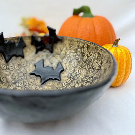 Ceramic candy bowl with halloween texture with bat accents on light background with pumpkins.