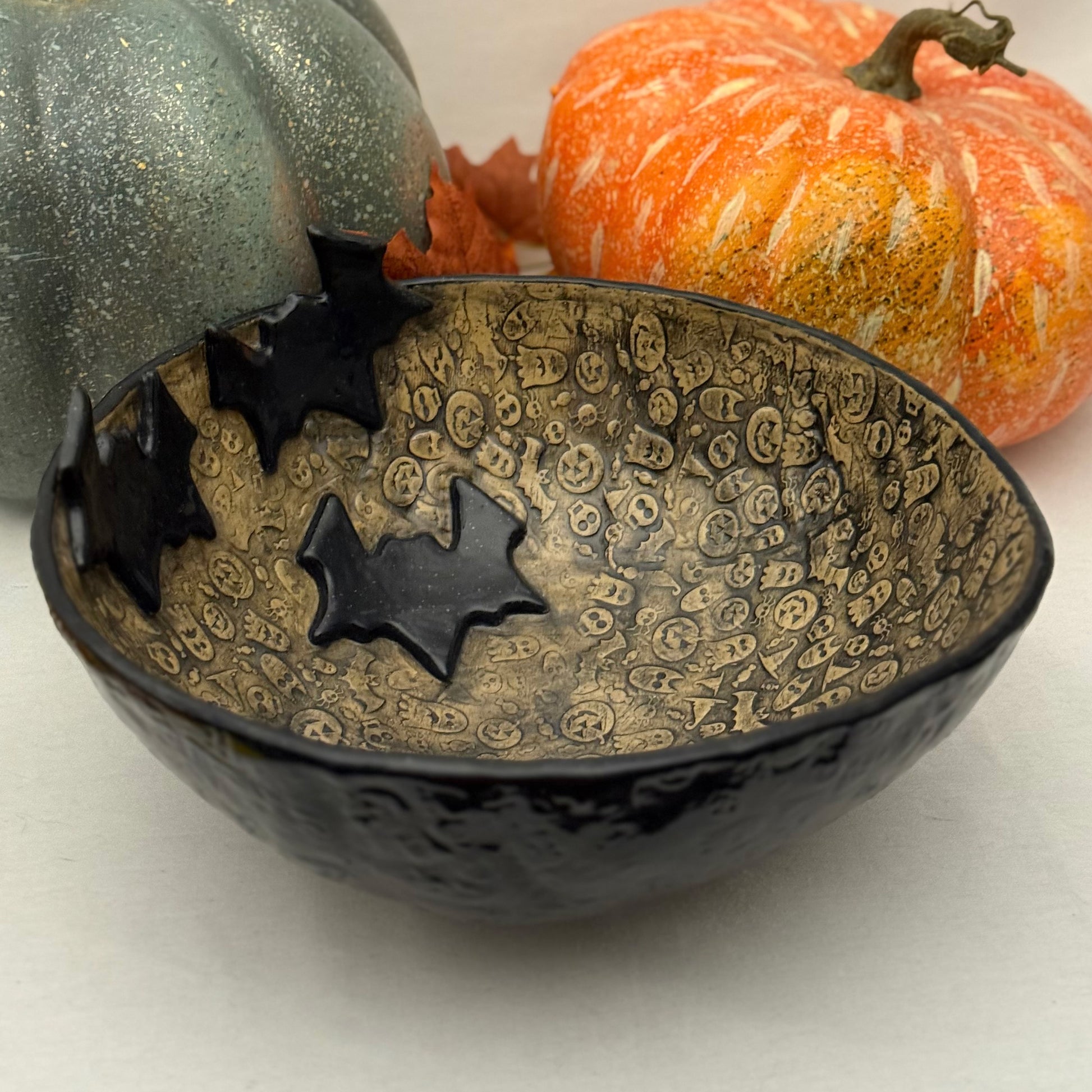 Ceramic candy bowl with halloween texture with bat accents on light background with pumpkins.