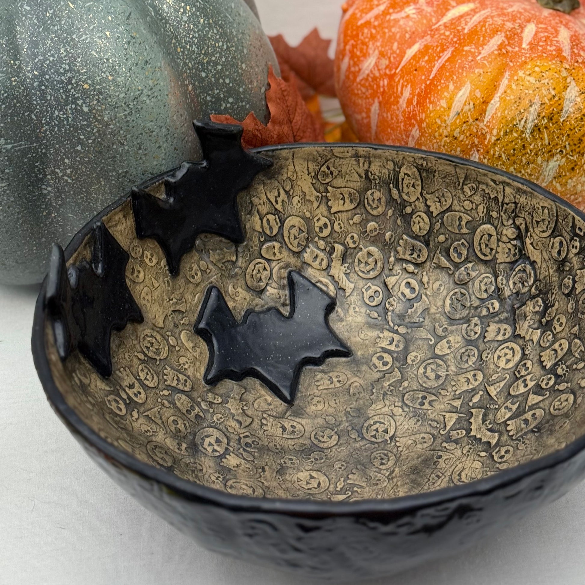 Ceramic candy bowl with halloween texture with bat accents on light background with pumpkins.