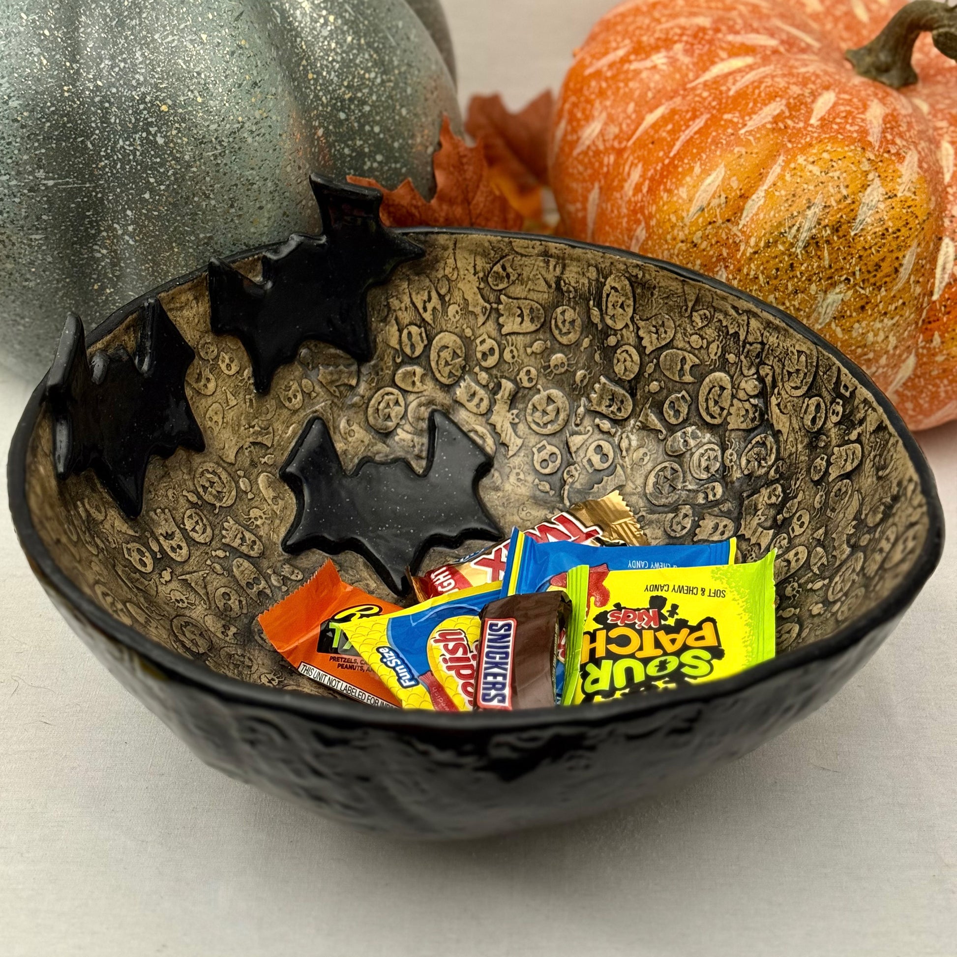 Ceramic candy bowl with halloween texture with bat accents on light background with pumpkins.