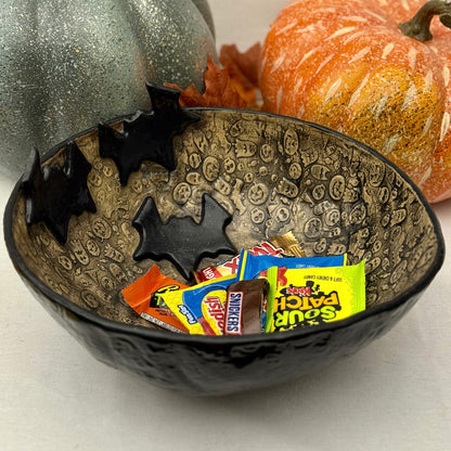 Ceramic candy bowl with halloween texture with bat accents on light background with pumpkins.