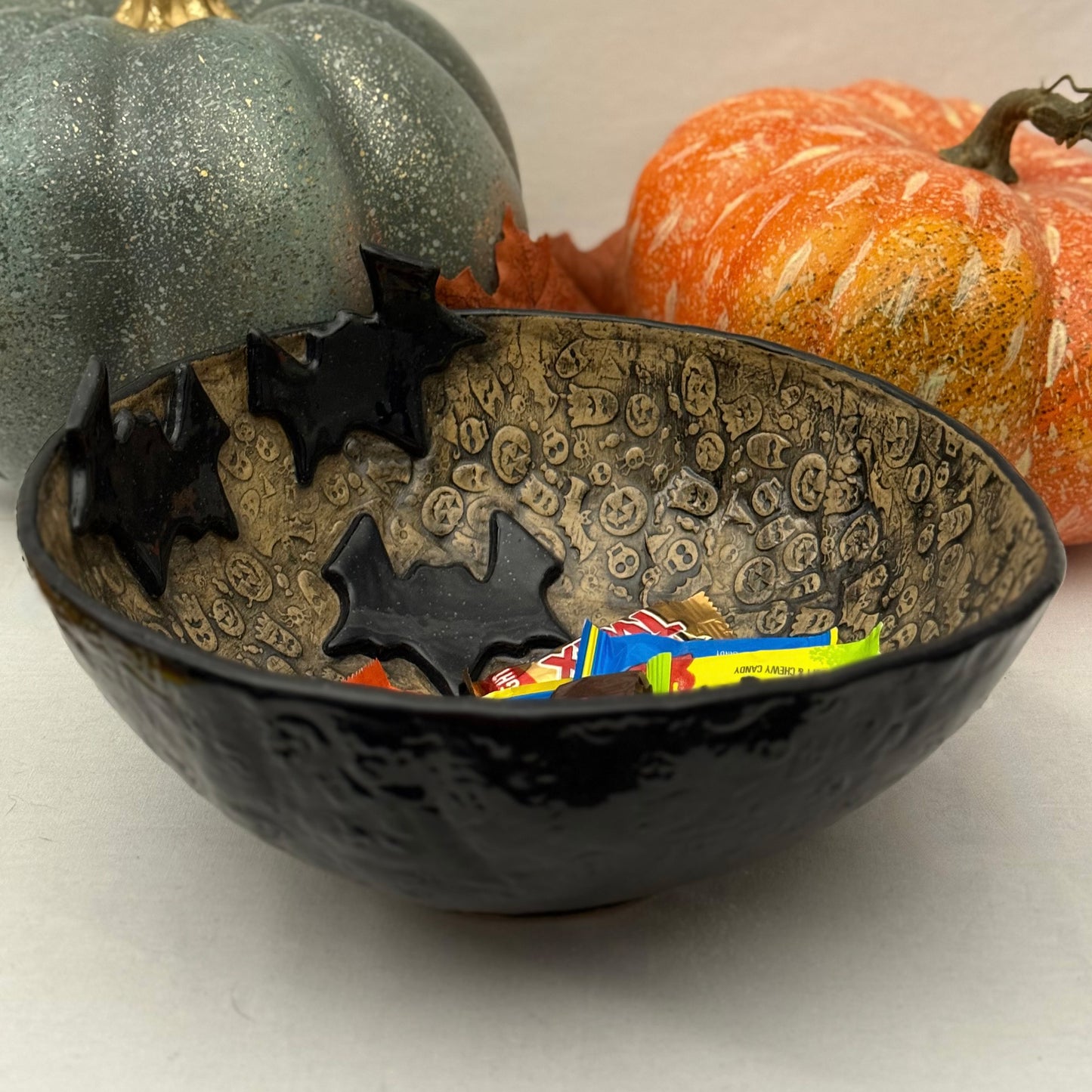Ceramic candy bowl with halloween texture with bat accents on light background with pumpkins.