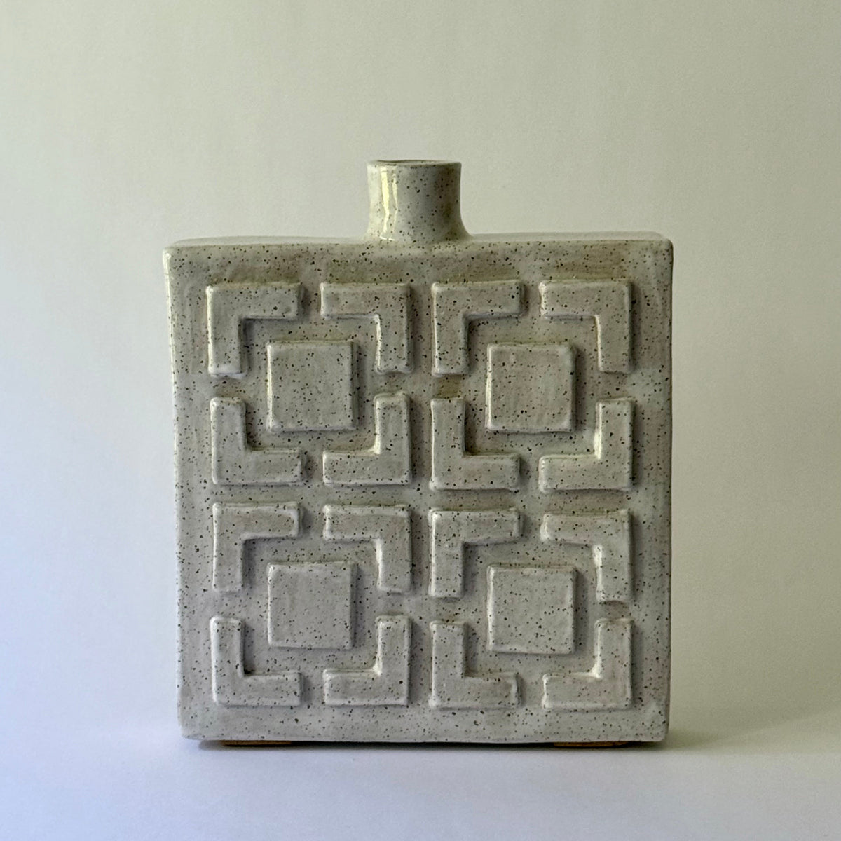 A rectangular ceramic vase with a short cylindrical neck and a raised geometric breeze block pattern on the front, shown on a plain light gray background.