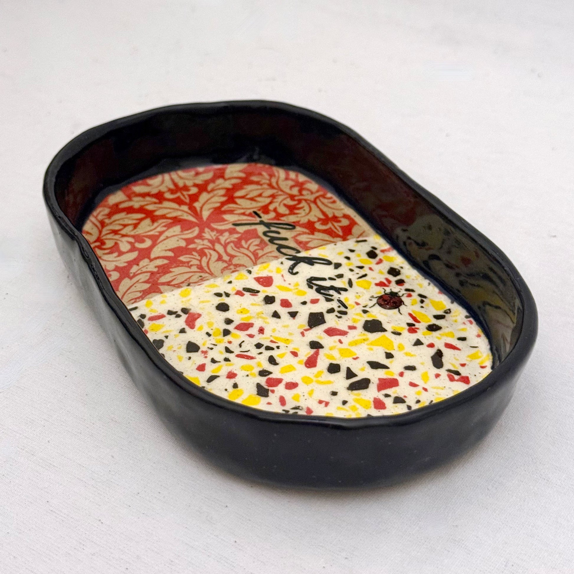 Decorative tray with damask pattern, black text, lady bug, and terrazzo design on a white background