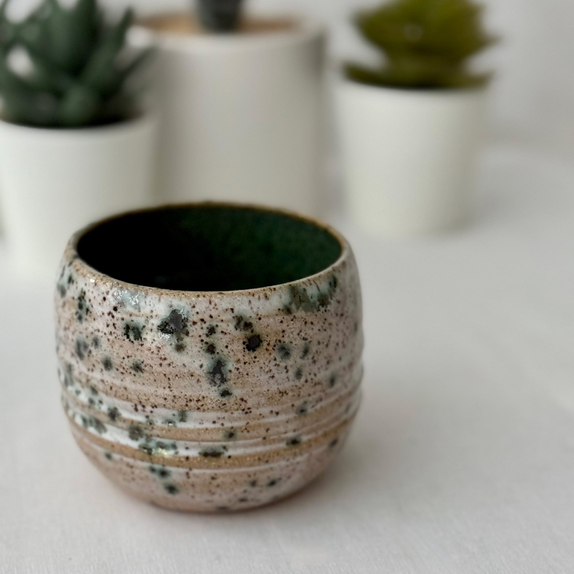 Speckled ceramic pot on a white surface with autumn leaves in the background