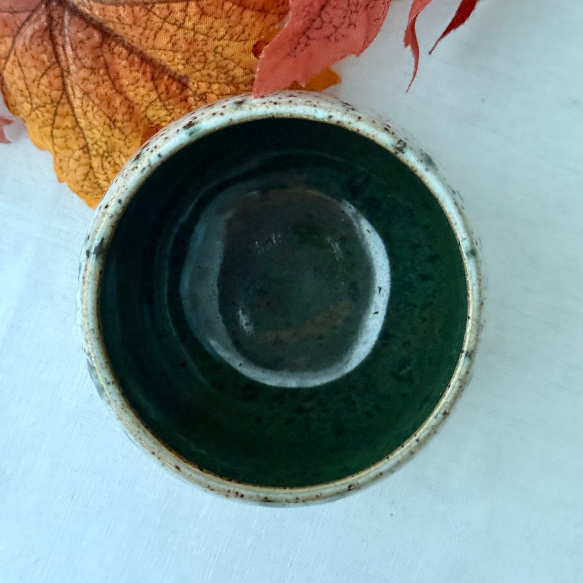 Speckled ceramic pot on a white surface with autumn leaves in the background