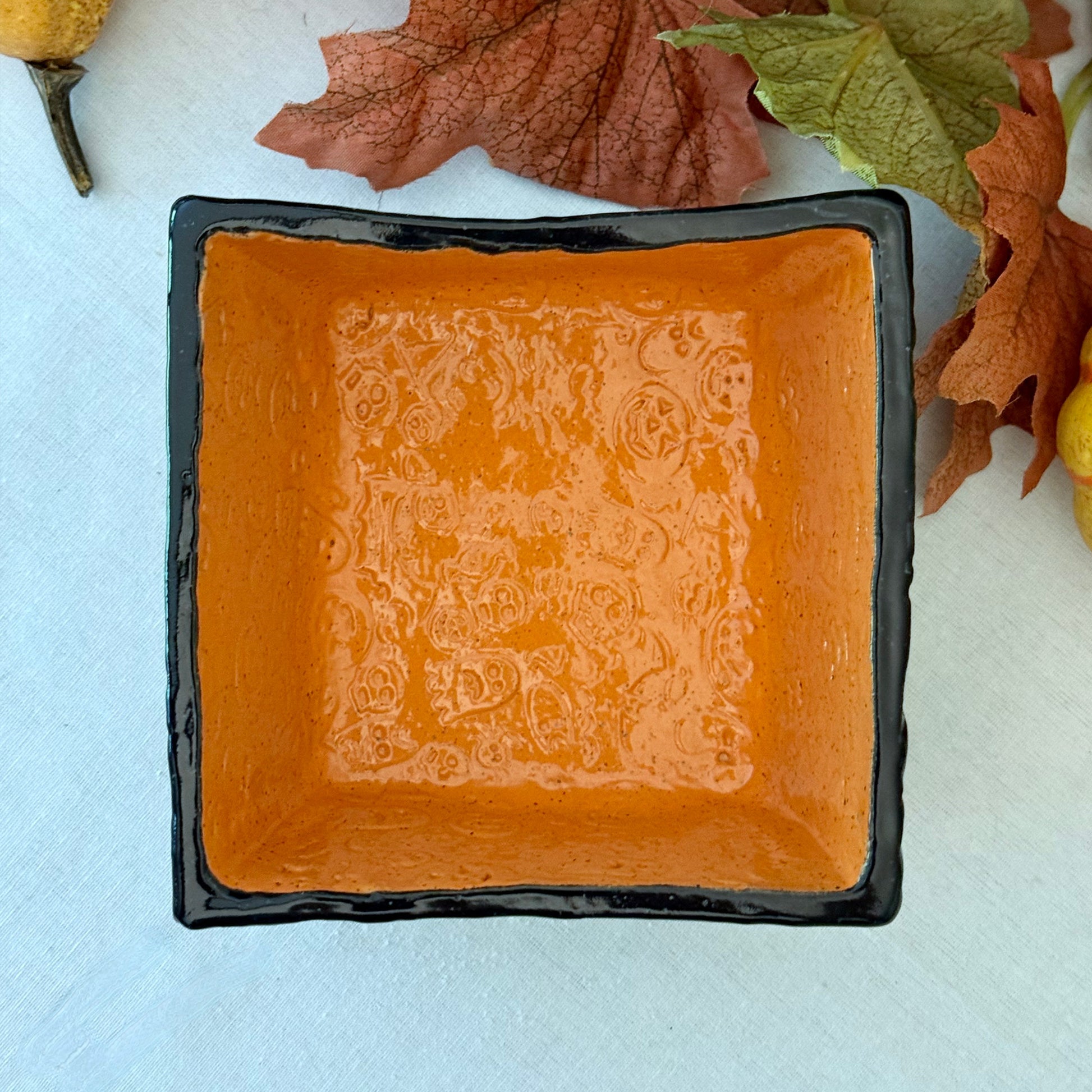 Square Halloween textured ceramic candy bowl on a white surface with pumpkins in the background.