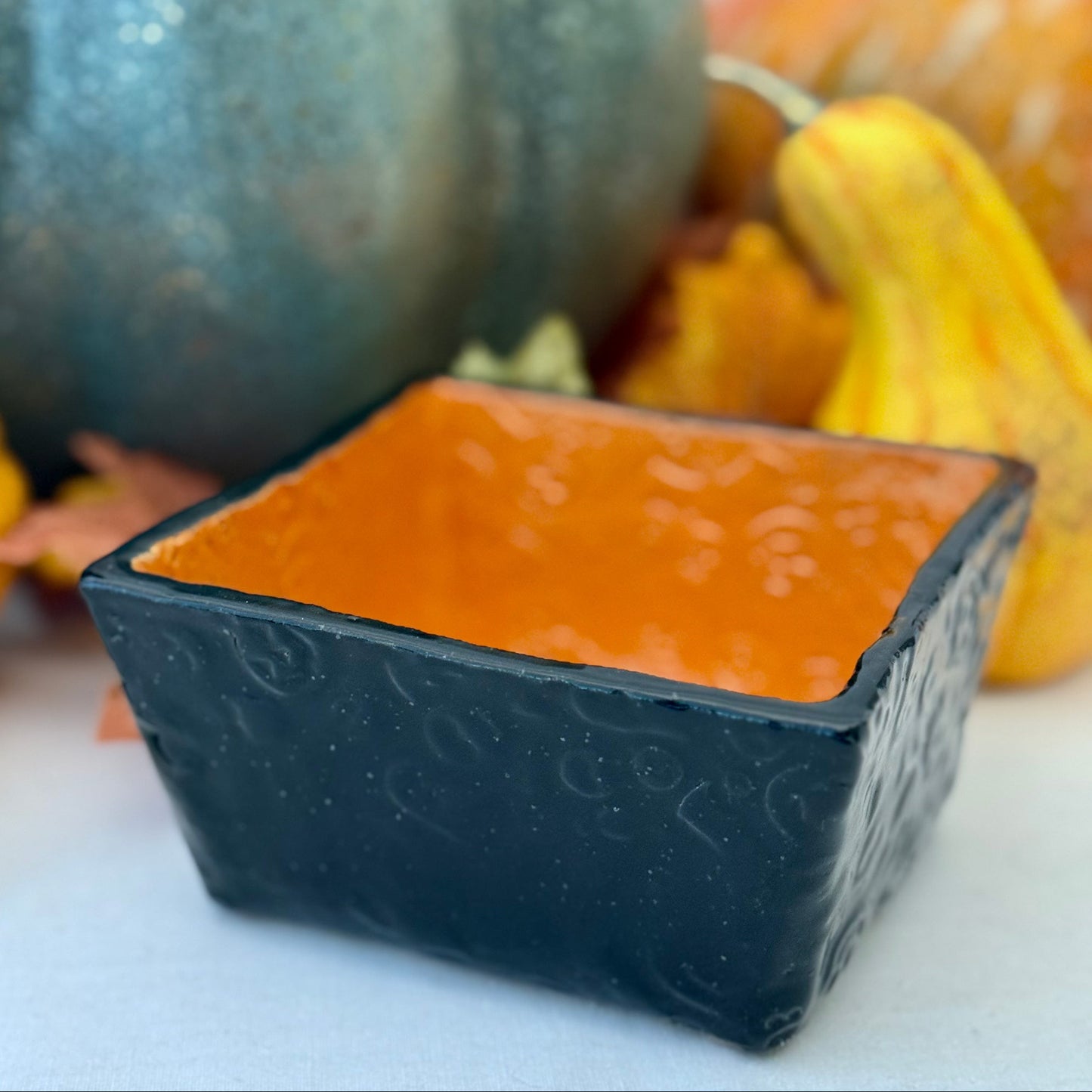 Square Halloween textured ceramic candy bowl  on a white surface with pumpkins in the background.