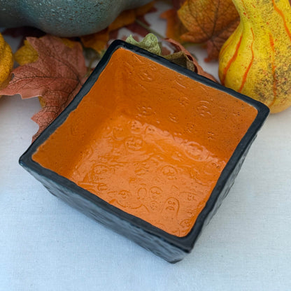 Square Halloween textured ceramic candy bowl  on a white surface with pumpkins in the background.