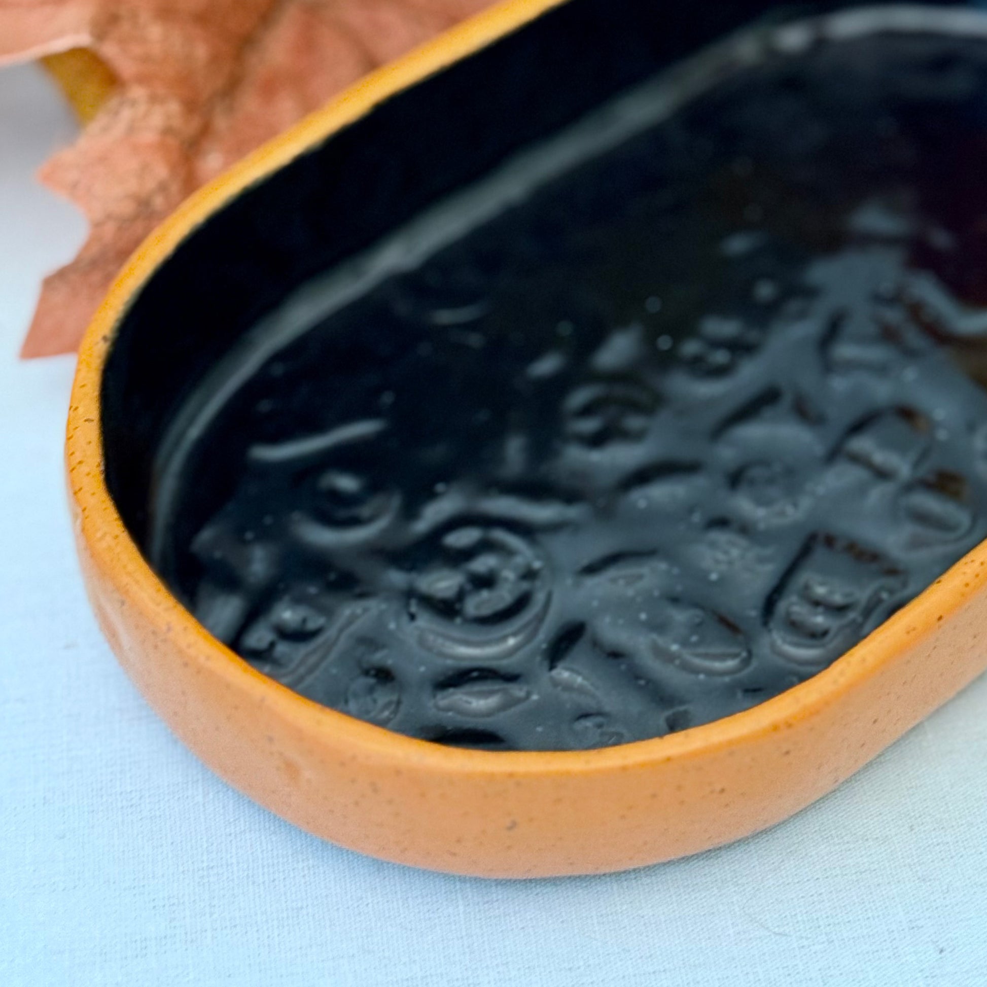 Black and orange Halloween textured oval trinket tray, surrounded by autumn leaves and a small pumpkin.