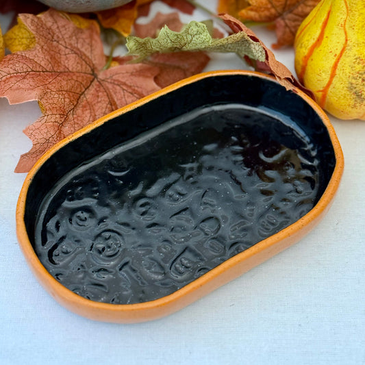 Black and orange Halloween textured oval trinket tray, surrounded by autumn leaves and a small pumpkin.