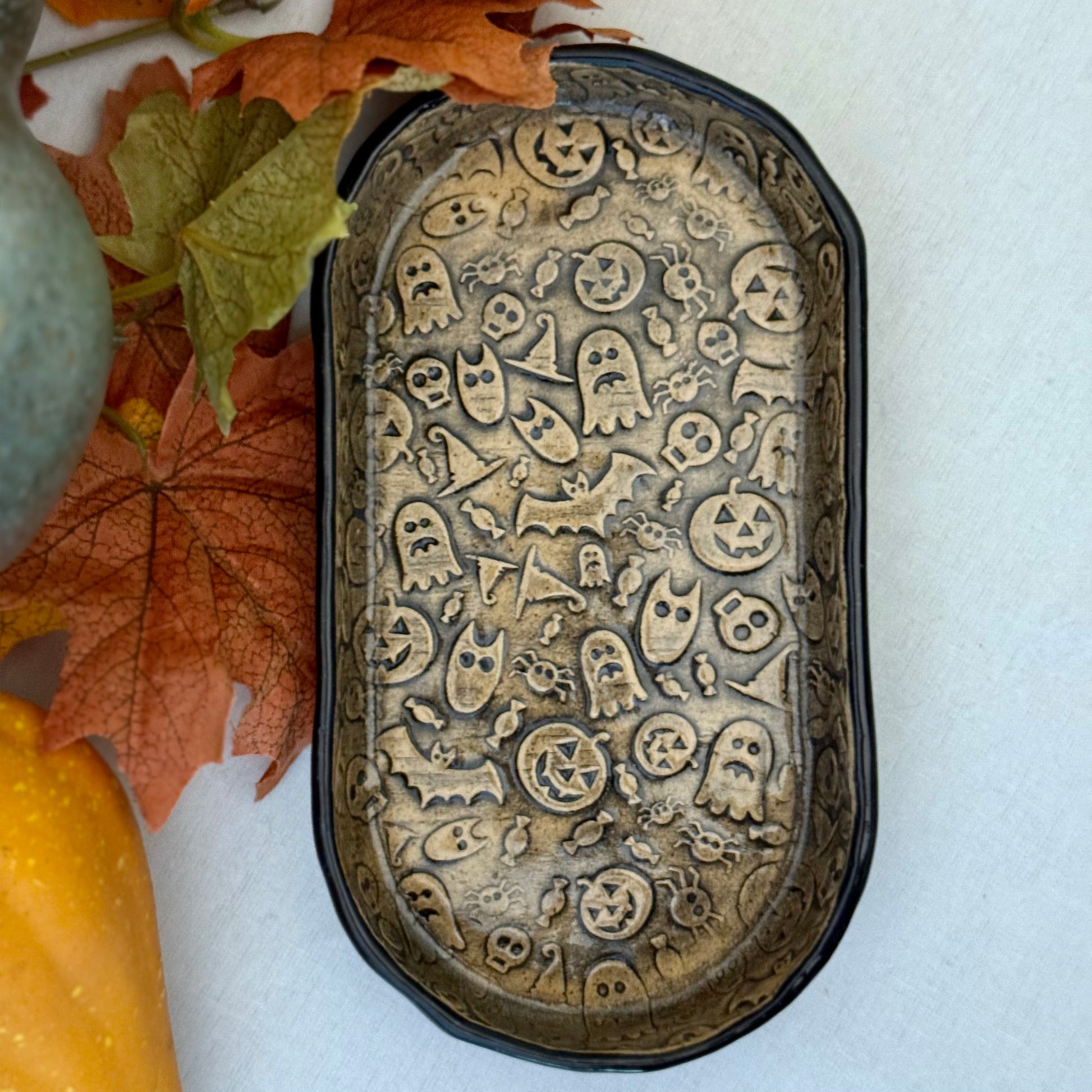 Decorative Halloween-themed ceramic tray with ghost, pumpkin, and skull designs on a white background.