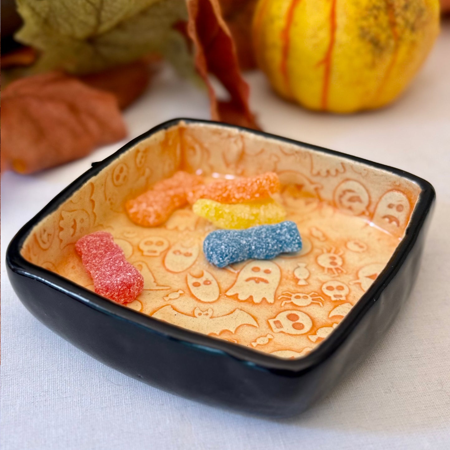 Decorative trinket dish with Halloween-themed design containing colorful gummy candy on a light background.