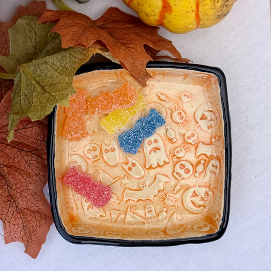 Decorative trinket dish with Halloween-themed design containing colorful gummy candy on a light background.