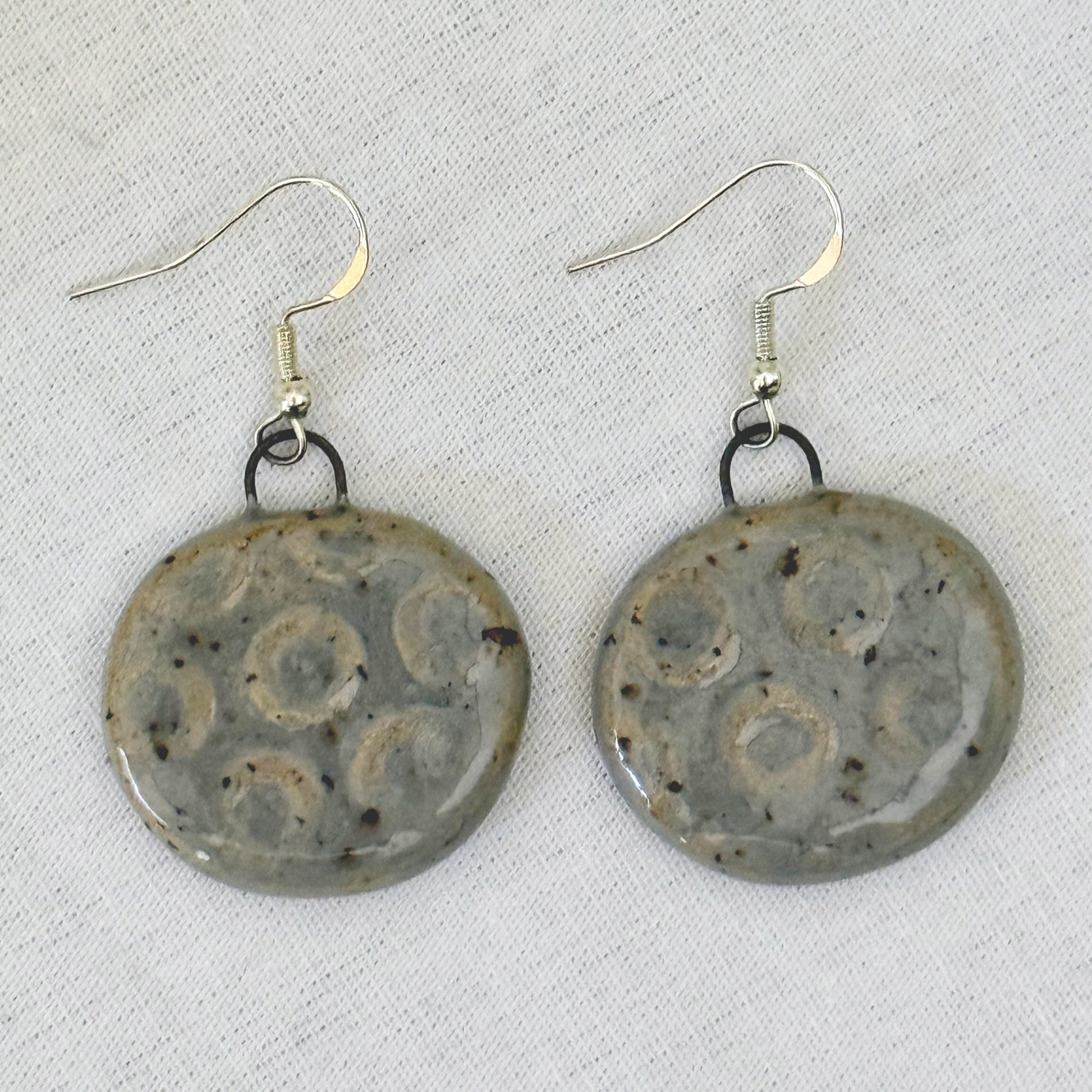 Pair of ceramic earrings with decorative patterns on a light background