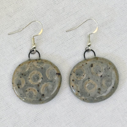 Pair of ceramic earrings with decorative patterns on a light background