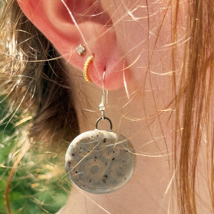 Close-up of a person wearing a round grey earring with a textured surface.