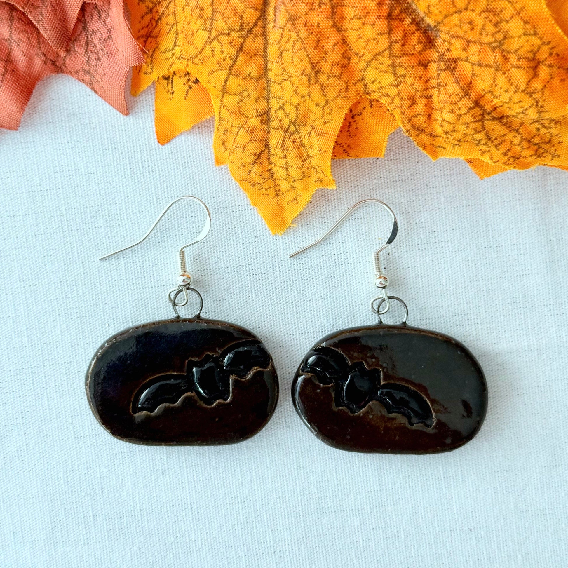 Black earrings with a bat design on a light background with orange leaves.