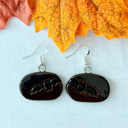 Black earrings with a bat design on a light background with orange leaves.