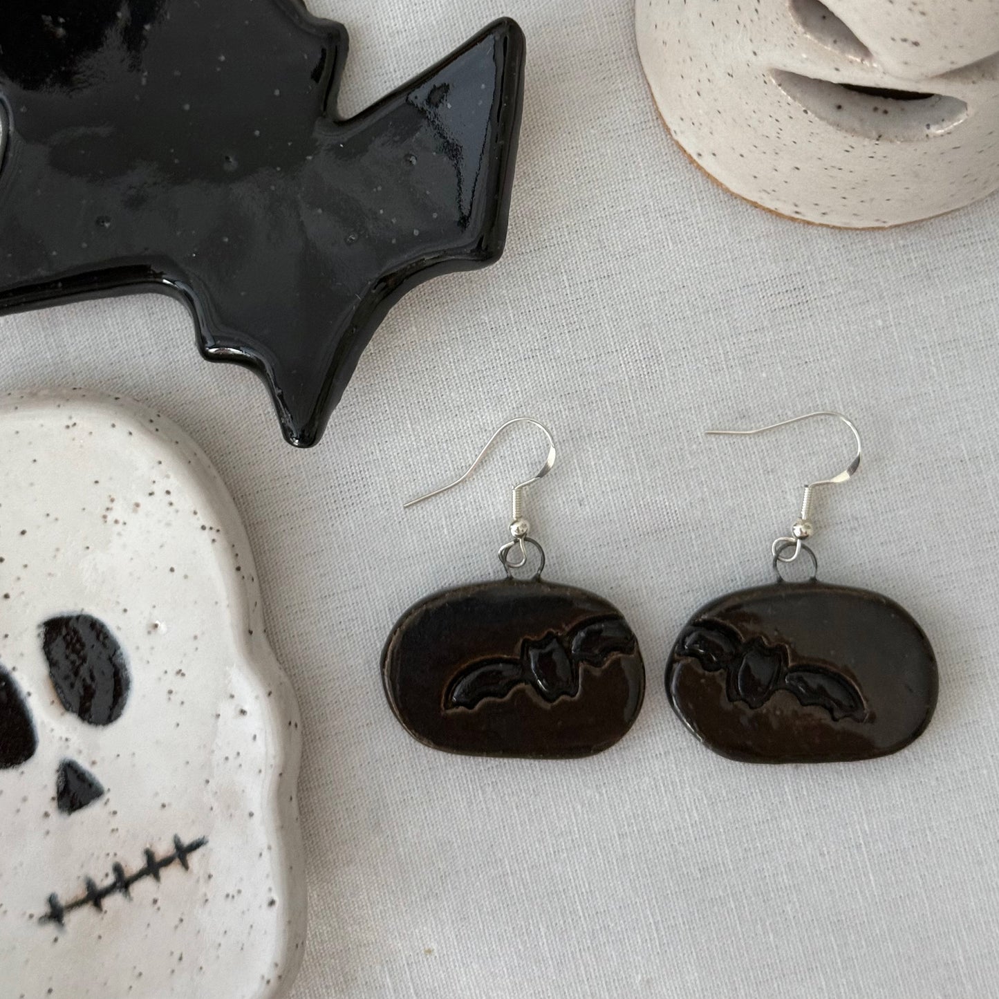 Black bat earrings on a textured surface with Halloween-themed decor.
