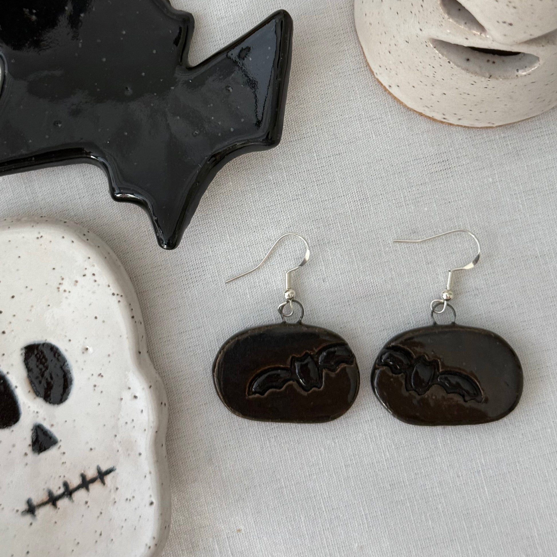 Black bat earrings on a textured surface with Halloween-themed decor.