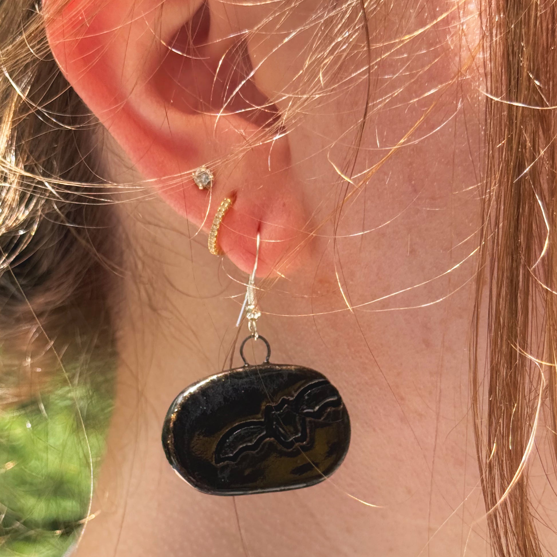 Close-up of an ear wearing a black dangling earring with a bat design.
