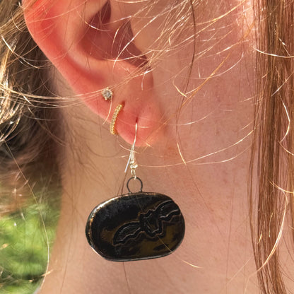 Close-up of an ear wearing a black dangling earring with a bat design.