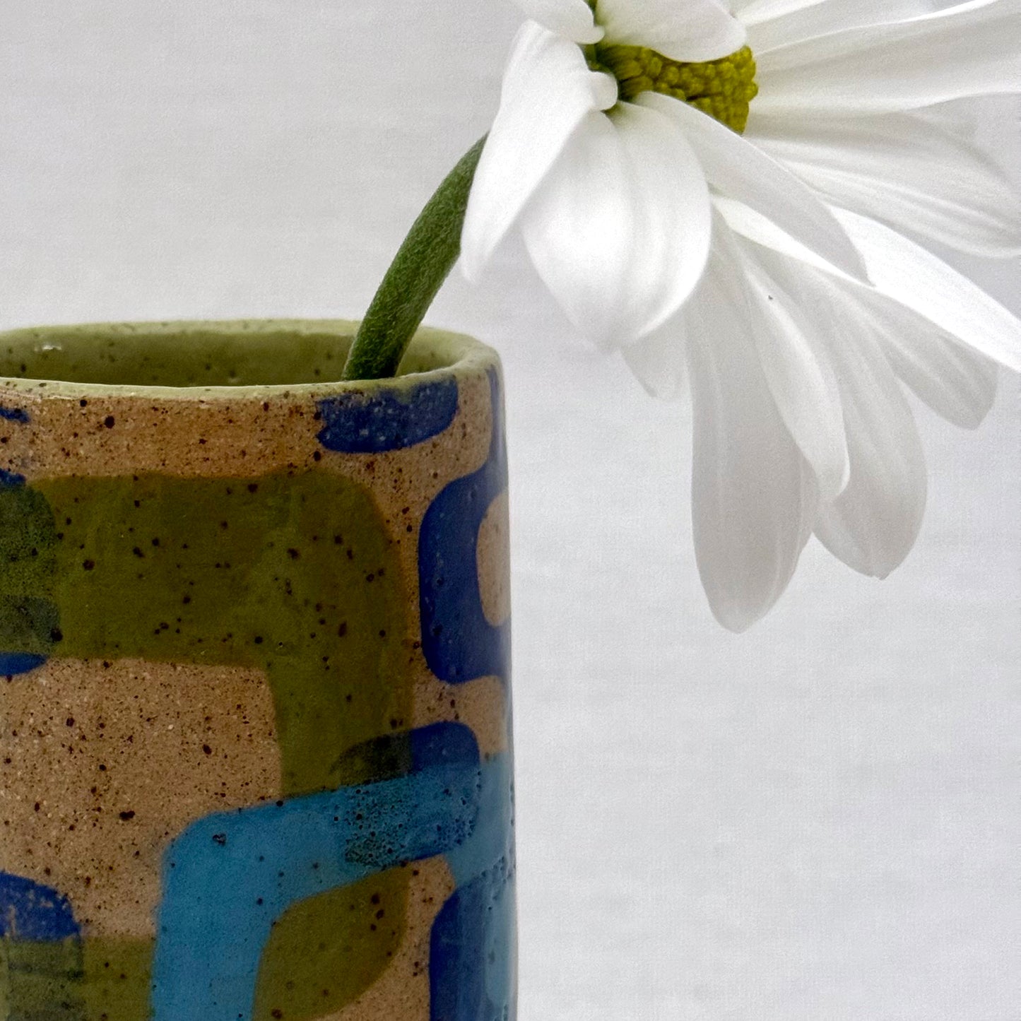 Ceramic vase with abstract patterns holding a white flower against a white background