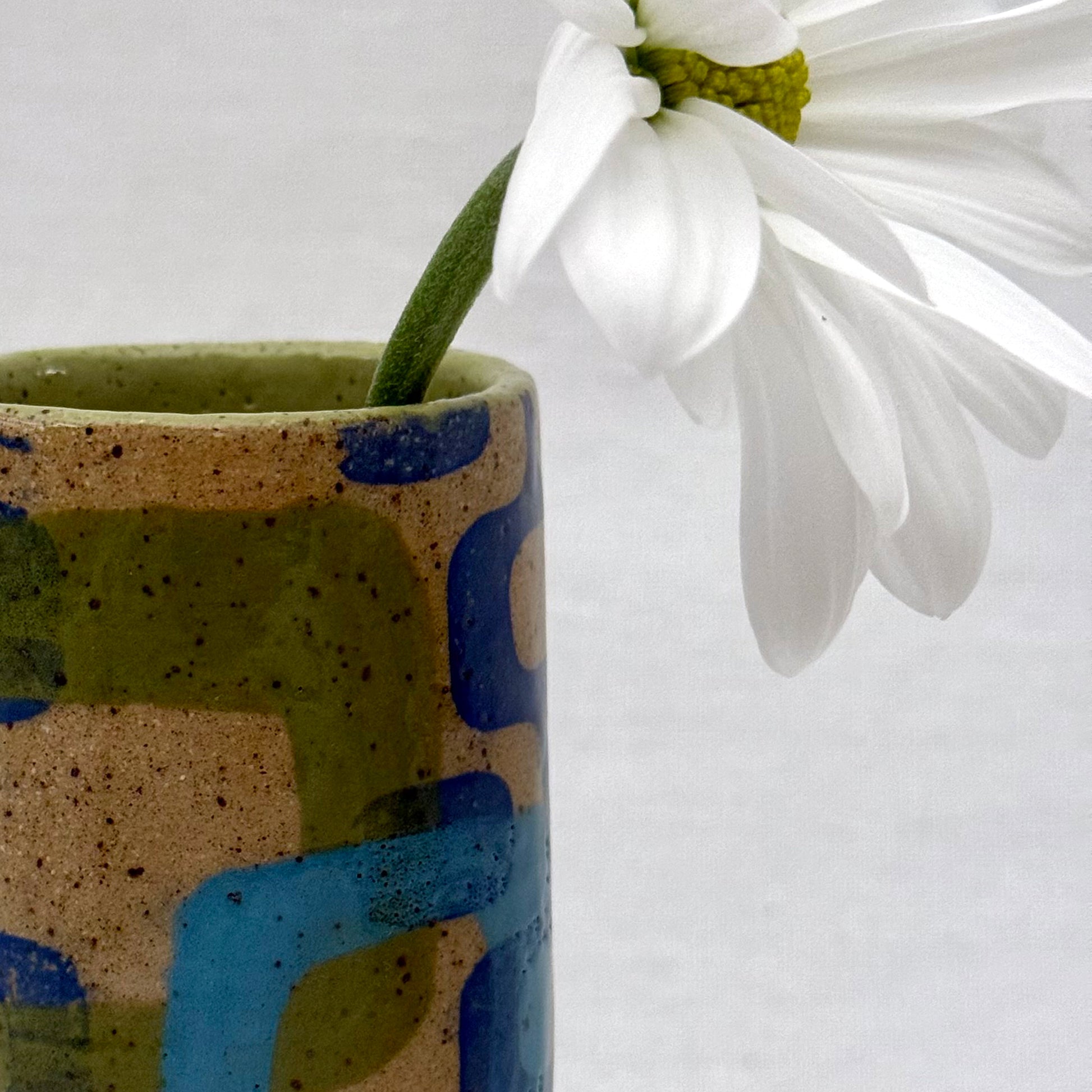 Ceramic vase with abstract patterns holding a white flower against a white background