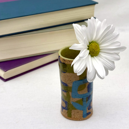 Blue and green vase with a white flower in front of stacked books on a white surface