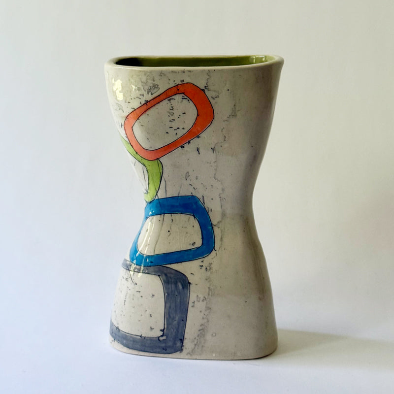 Handmade ceramic vase with interconnected geometric shapes in blue, coral, green, and gray on a sculptural hourglass silhouette.