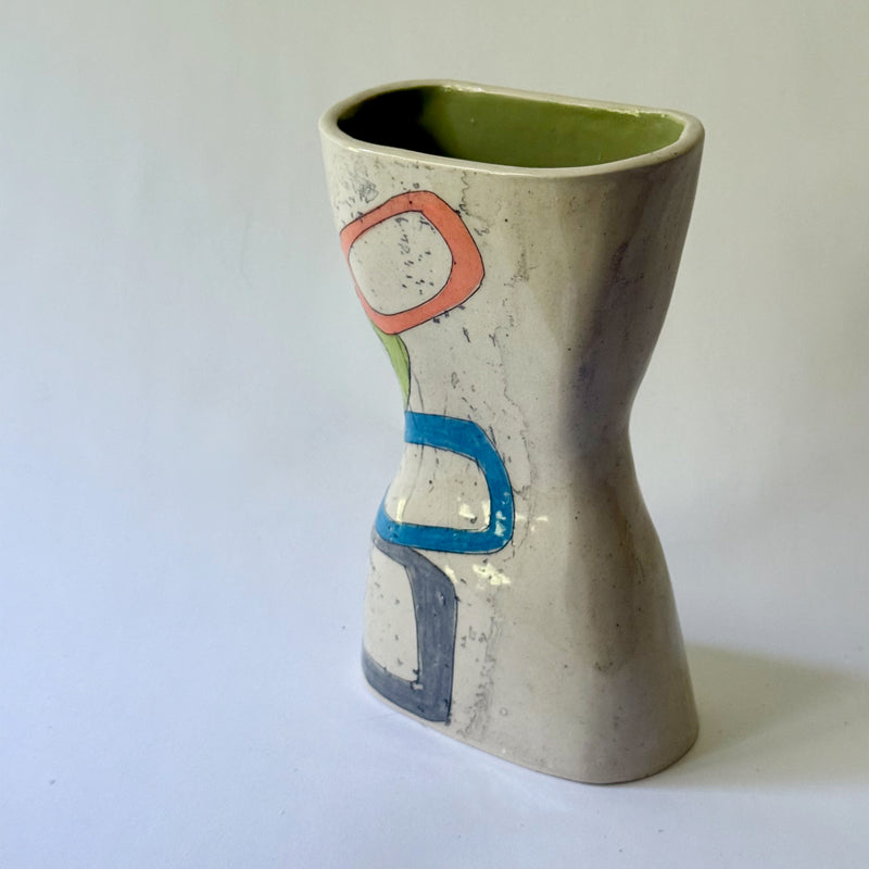Handmade ceramic vase with interconnected geometric shapes in blue, coral, green, and gray on a sculptural hourglass silhouette.