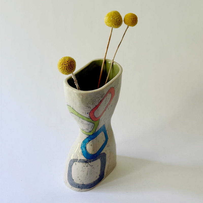 Handmade ceramic vase with interconnected geometric shapes in blue, coral, green, and gray on a sculptural hourglass silhouette.