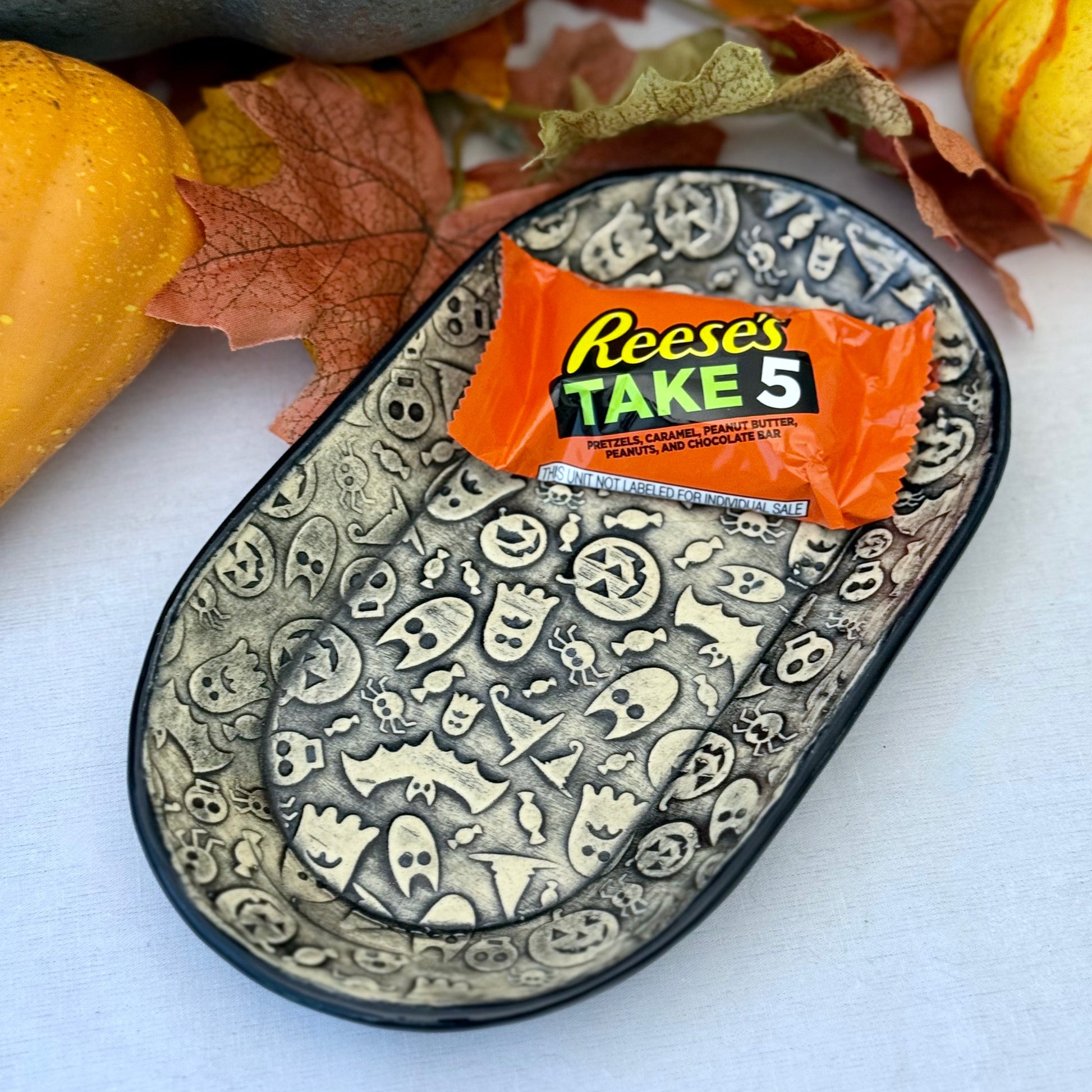 Halloween themed oval plate with a candy bar on light background with leaves and pumpkins
