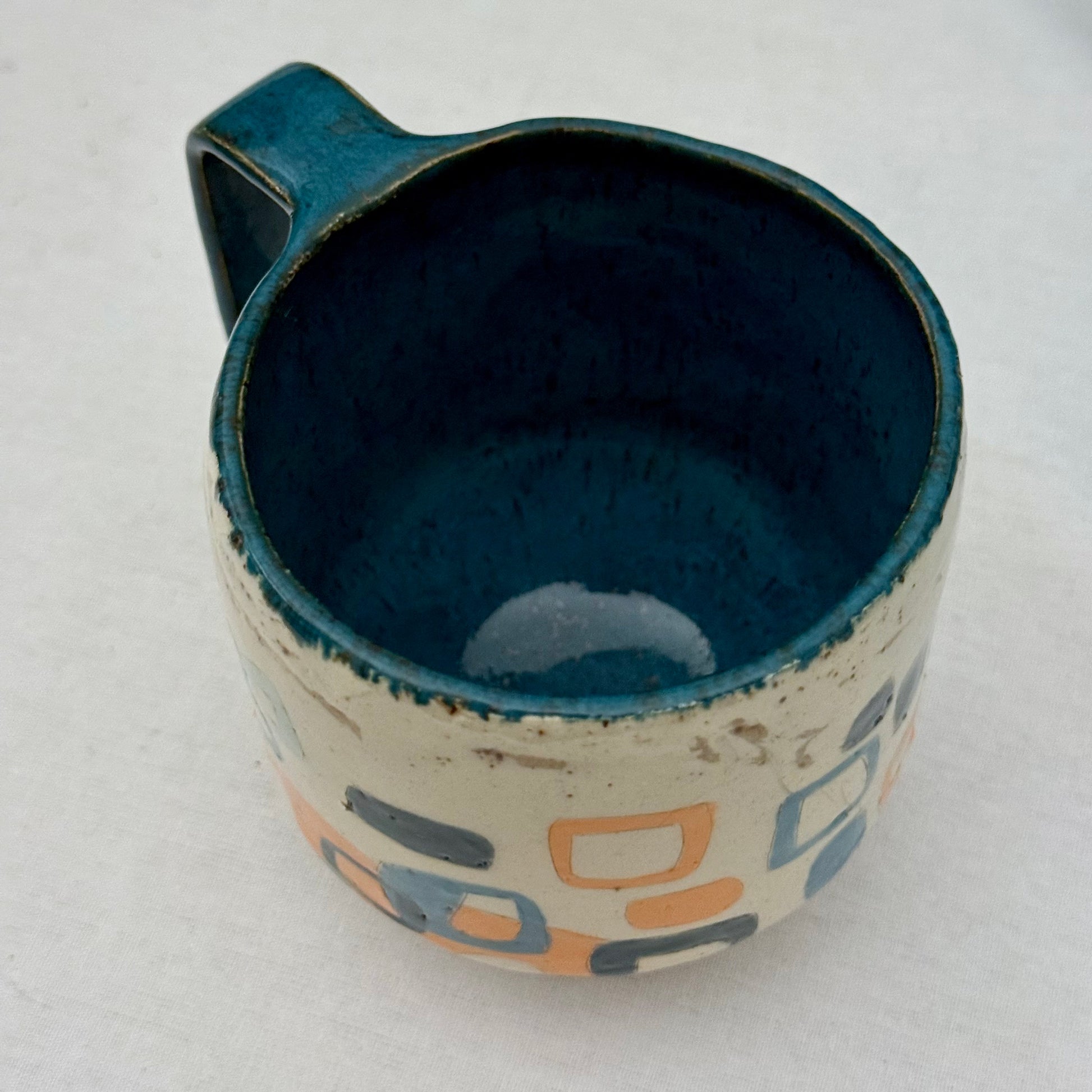 Ceramic mug with blue interior and geometric pattern on exterior against a white background