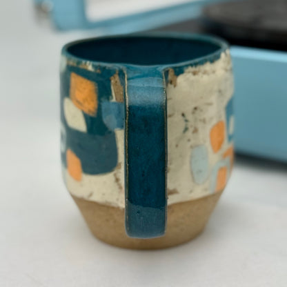 Ceramic mug with blue handle and abstract pattern on a white surface