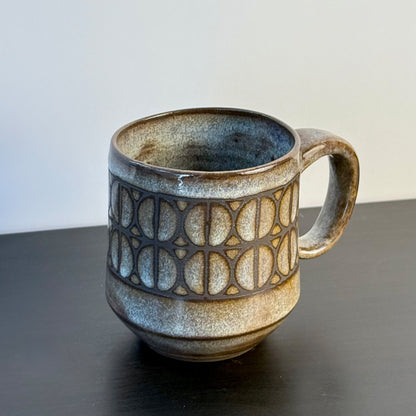 Handmade ceramic mug with a repeating Split Circle breeze block pattern, dark clay showing through the design, and a warm earthy glaze.