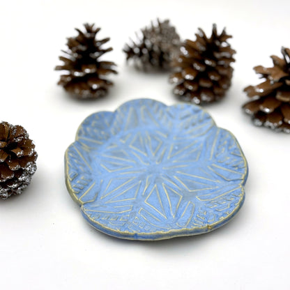 Blue ceramic plate with geometric snowflake pattern on a white background with pinecones