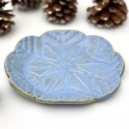 Blue ceramic plate with geometric snowflake pattern on a white background with pinecones